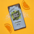 A bar of Seed and Bean Vegan Sea Salt and Orange Milk Chocolate on an orange background with orange slices and sea salt.